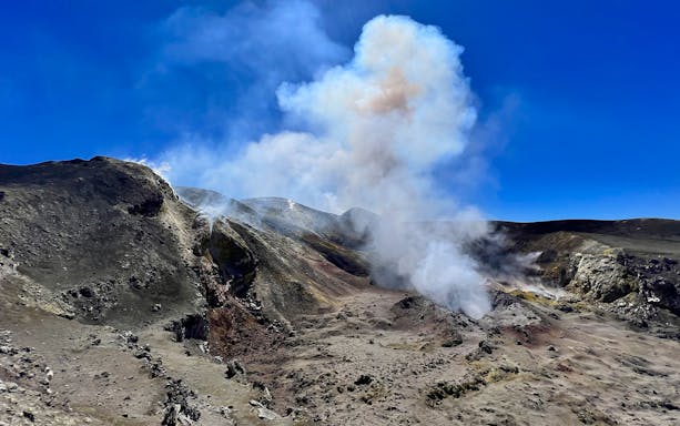 Mount Etna summit with smoke rising from volcanic crater under clear blue sky.