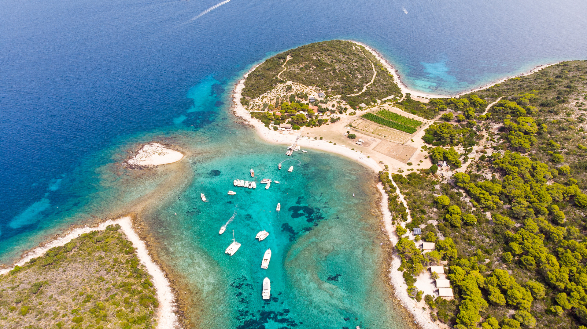 Aerial view of Budikovac Island with boats in turquoise waters and lush greenery.