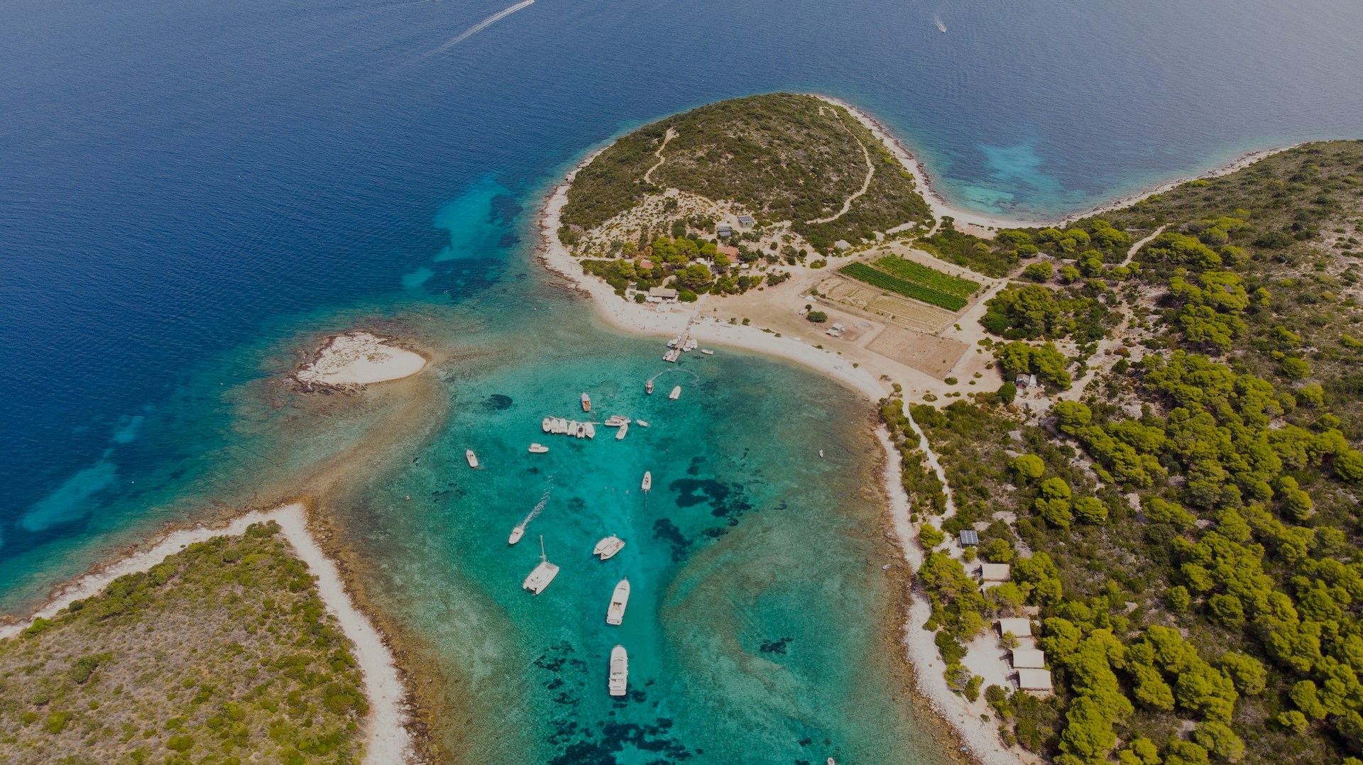 Aerial view of Budikovac Island with boats in turquoise waters and lush greenery.