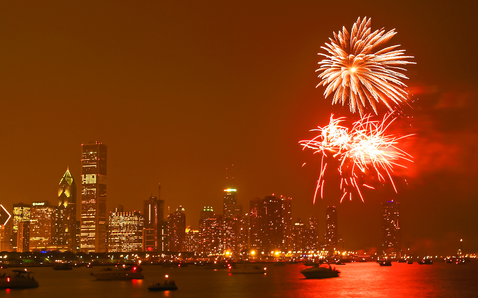 Fireworks over Chicago skyline at night with boats on Lake Michigan.