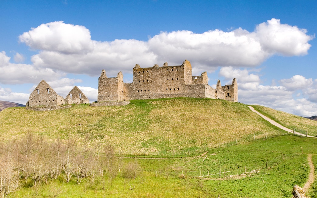 Ruthven Barracks ruins on a grassy hill under a blue sky in Scotland.