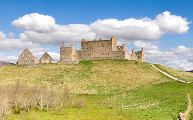 Ruthven Barracks ruins on a grassy hill under a blue sky in Scotland.