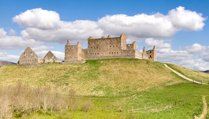 Ruthven Barracks ruins on a grassy hill under a blue sky in Scotland.