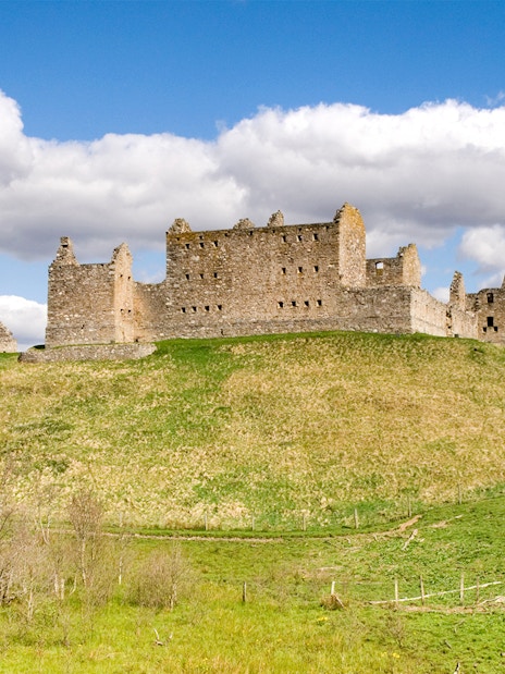 Ruthven Barracks ruins on a grassy hill under a blue sky in Scotland.