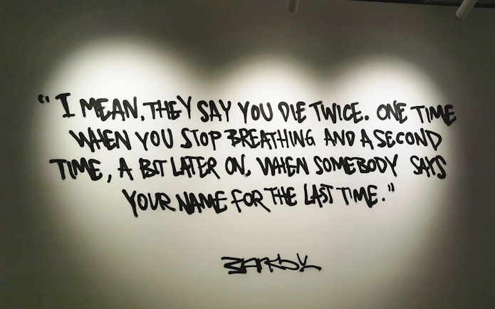 Banksy artwork with quote about dying twice, displayed on a wall.