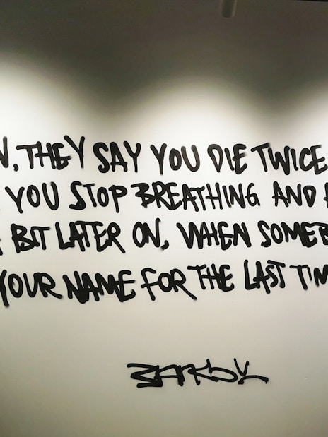 Banksy artwork with quote about dying twice, displayed on a wall.