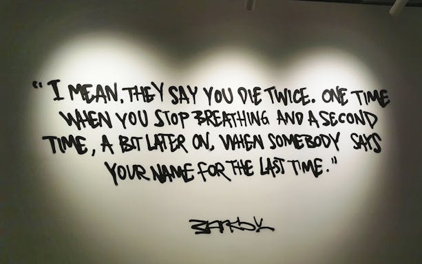 Banksy artwork with quote about dying twice, displayed on a wall.