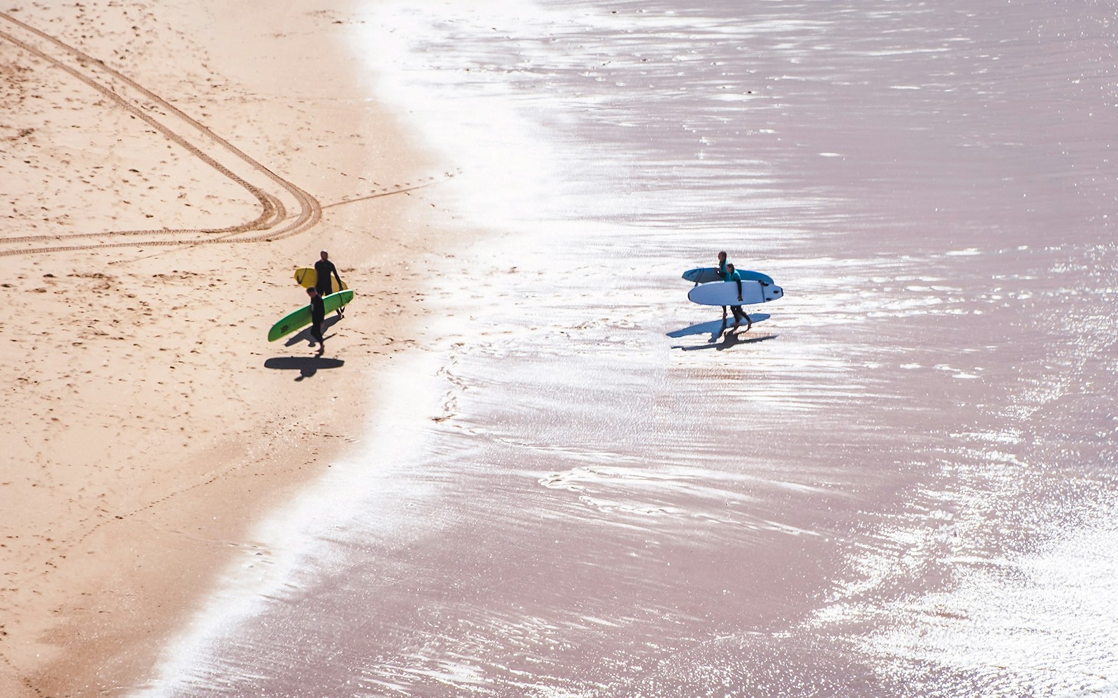Surfers carrying boards along a sandy beach shore.