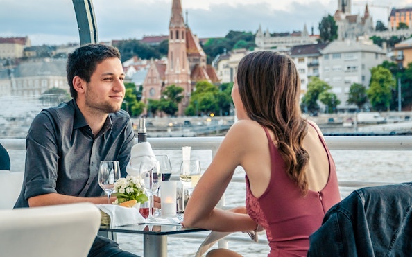 Couple enjoying a candlelit dinner on a Budapest river cruise with cityscape views.
