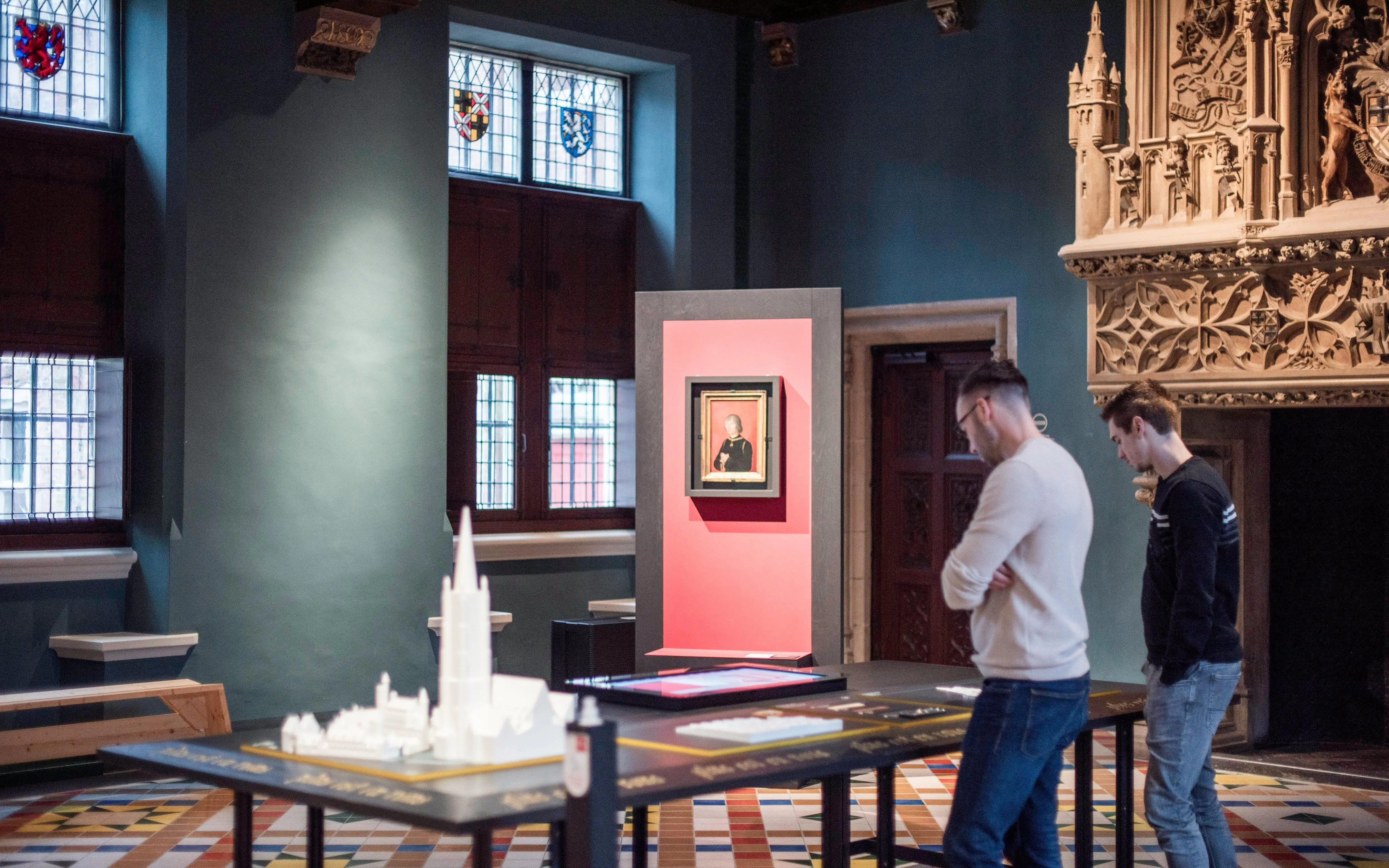 Visitors observing exhibits at Gruuthusemuseum, Bruges, with historical artifacts and stained glass windows.