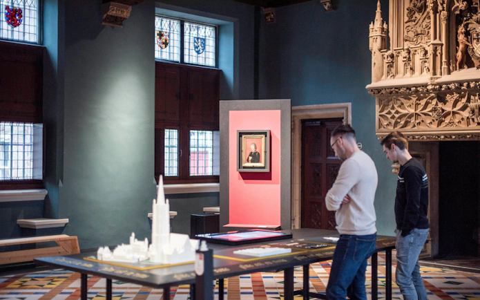 Visitors observing exhibits at Gruuthusemuseum, Bruges, with historical artifacts and stained glass windows.