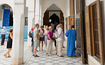 Tourists exploring Ben Youssef Medersa courtyard, Marrakech.