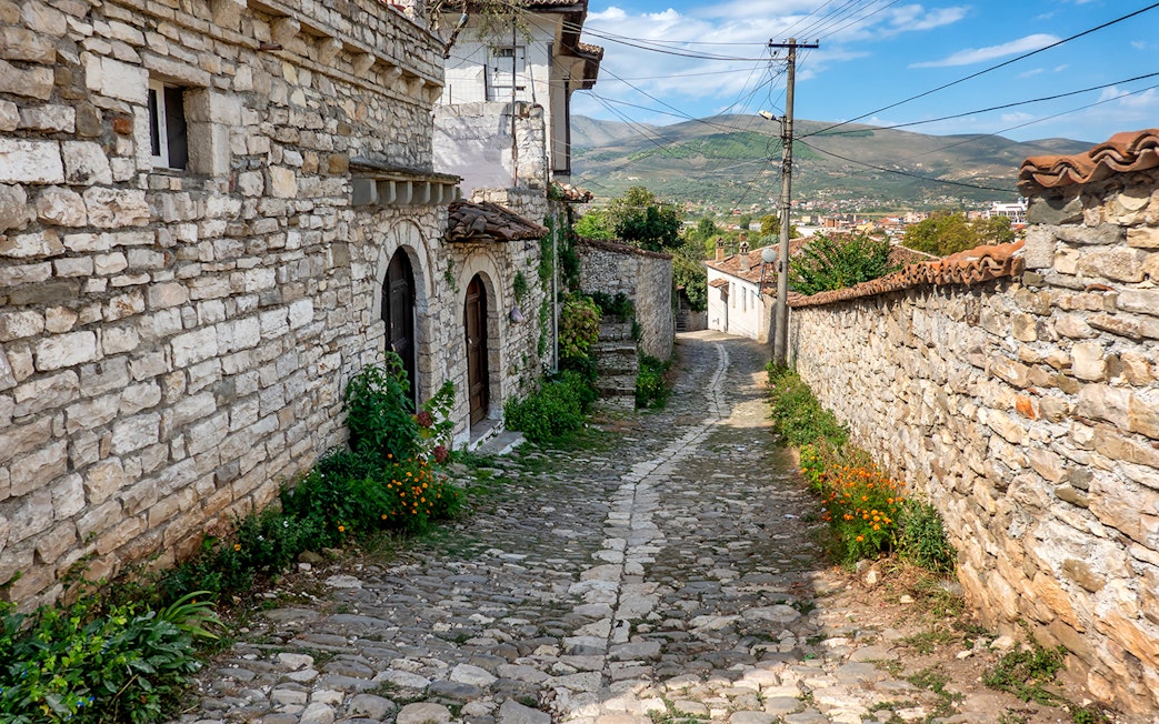 Cobblestone street in Old Town Berat with stone buildings and distant hills.