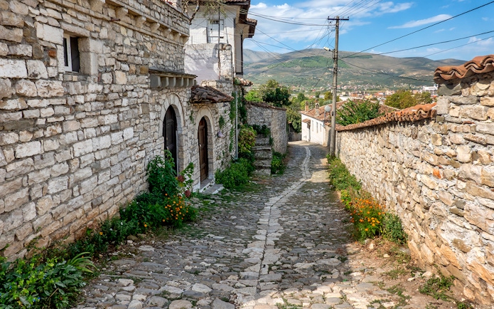 Cobblestone street in Old Town Berat with stone buildings and distant hills.