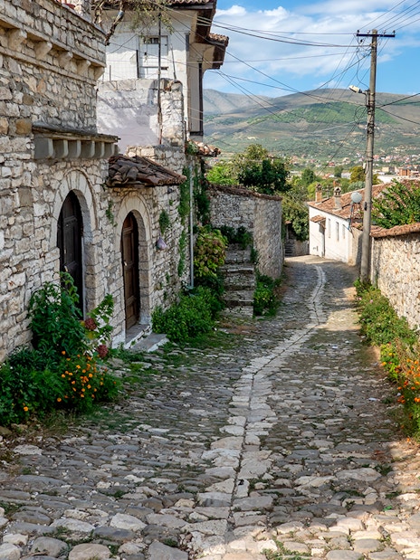 Cobblestone street in Old Town Berat with stone buildings and distant hills.