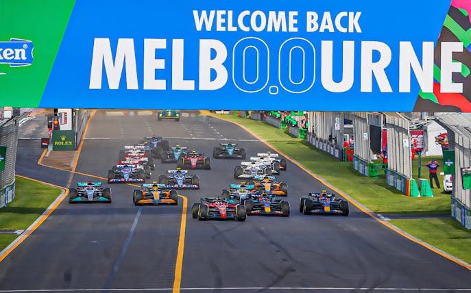 Formula 1 cars racing under "Welcome Back Melbourne" sign at Australian Grand Prix 2023.