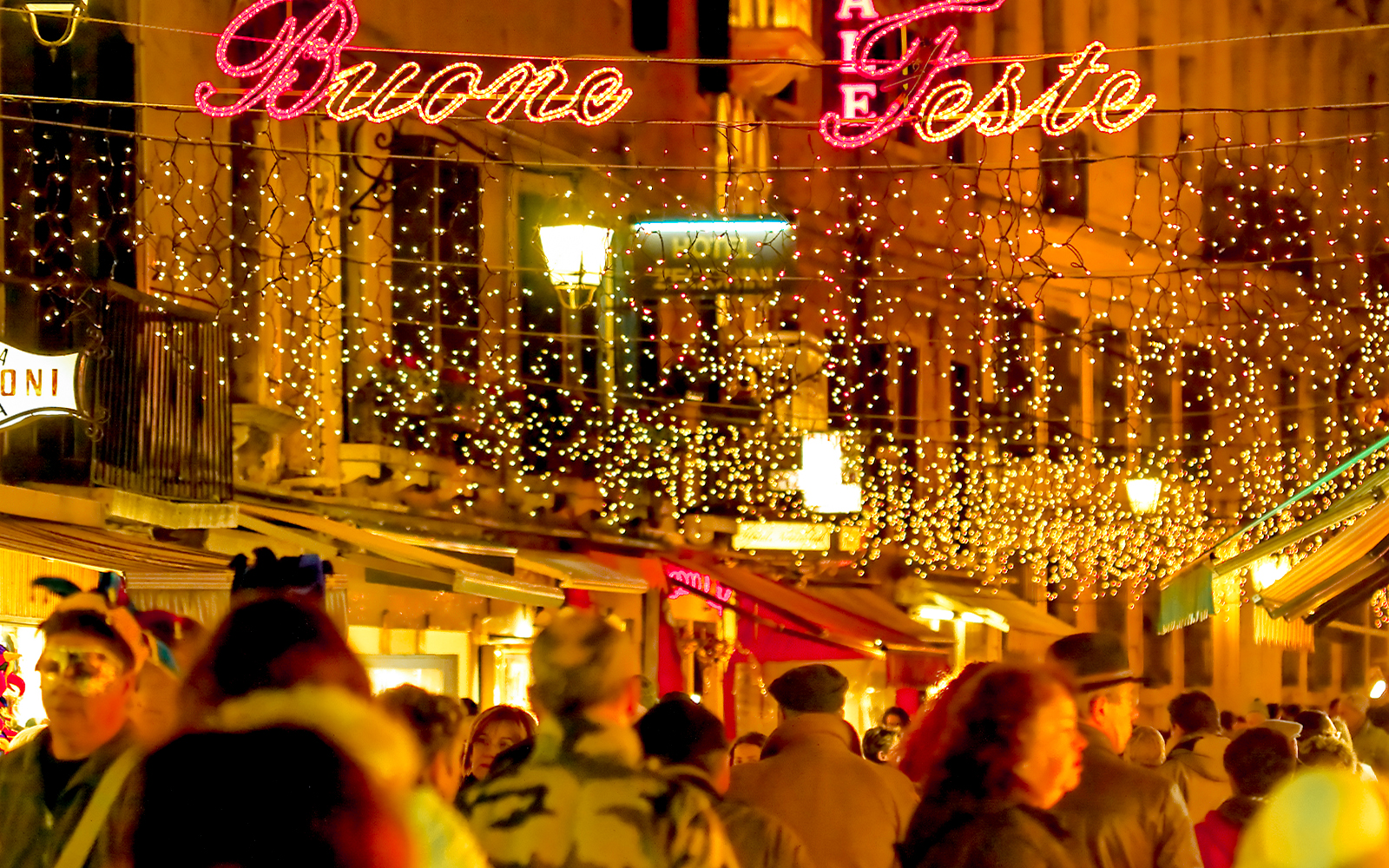 Venice street decorated with Christmas lights and "Buone Feste" sign, crowded with people.
