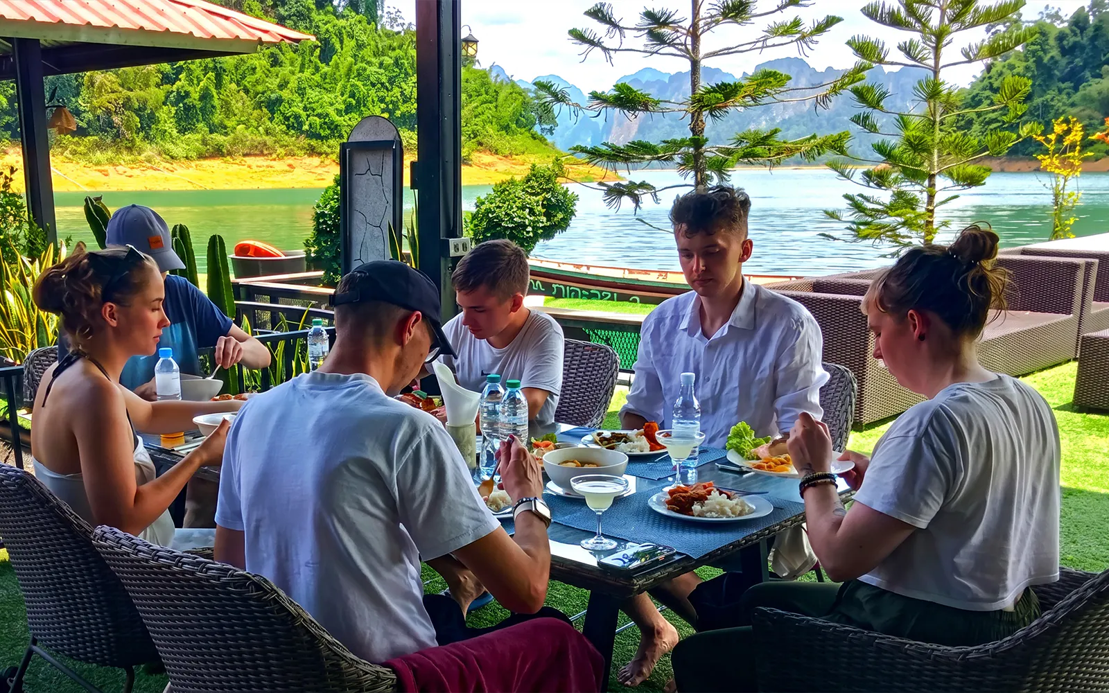 Tourists dining by Cheow Lan Lake with lush jungle and mountains in the background, Krabi boat tour.