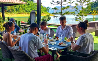 Tourists dining by Cheow Lan Lake with lush jungle and mountains in the background, Krabi boat tour.