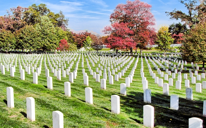 Rows of white headstones at Arlington National Cemetery, Washington DC, with autumn trees.