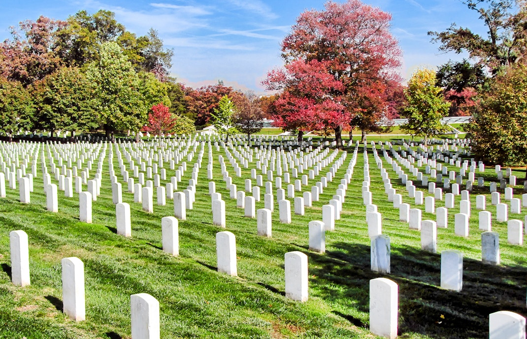 Rows of white headstones at Arlington National Cemetery, Washington DC, with autumn trees.