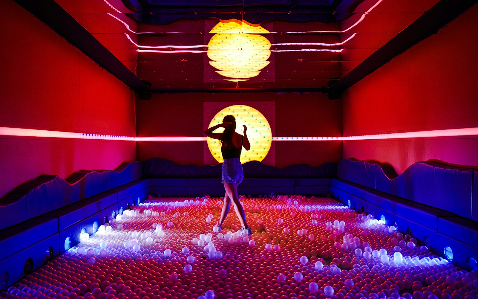 Person exploring vibrant ball pit with neon lights at Sunset Lagoon, Dopamine Land.