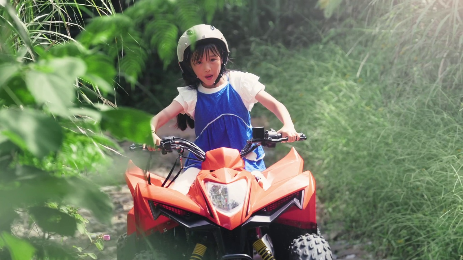 Child riding an ATV through lush greenery at JUNGLIA OKINAWA Park.