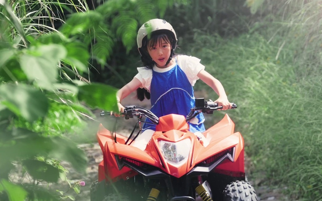 Child riding an ATV through lush greenery at JUNGLIA OKINAWA Park.