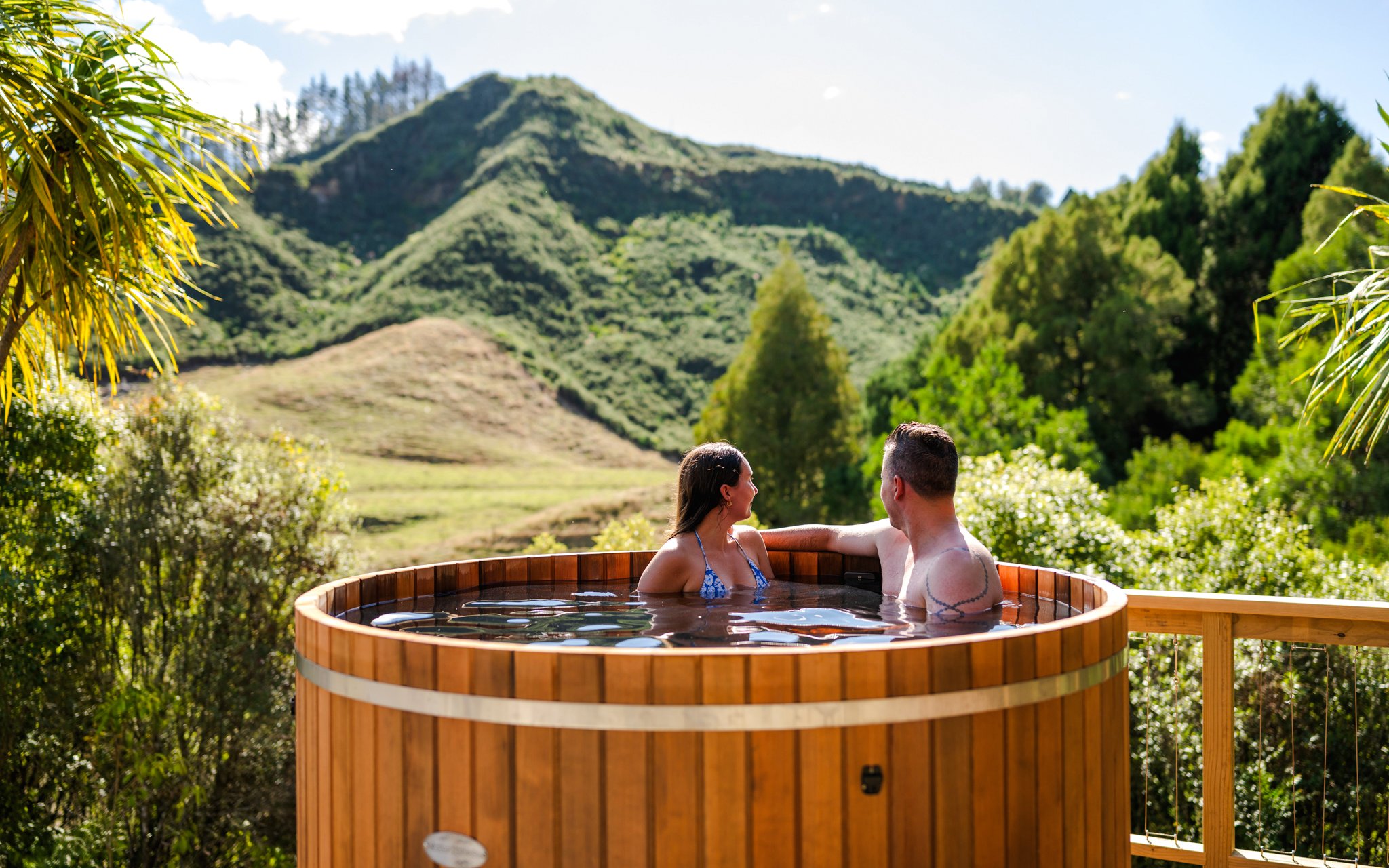 Couple relaxing in a hot tub with scenic view of lush hills at Waitomo, New Zealand.