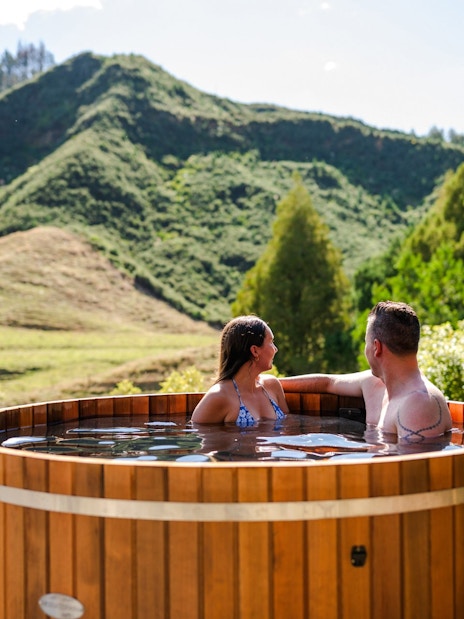 Couple relaxing in a hot tub with scenic view of lush hills at Waitomo, New Zealand.
