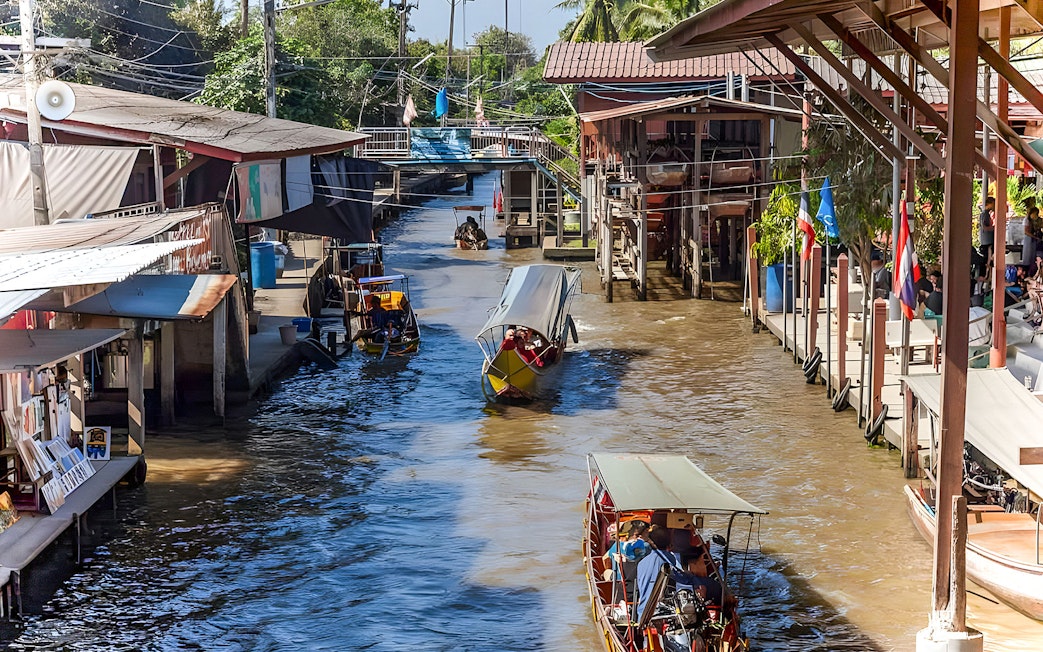 Boats navigating a bustling floating market canal with shops on both sides.