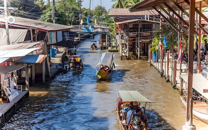 Boats navigating a bustling floating market canal with shops on both sides.