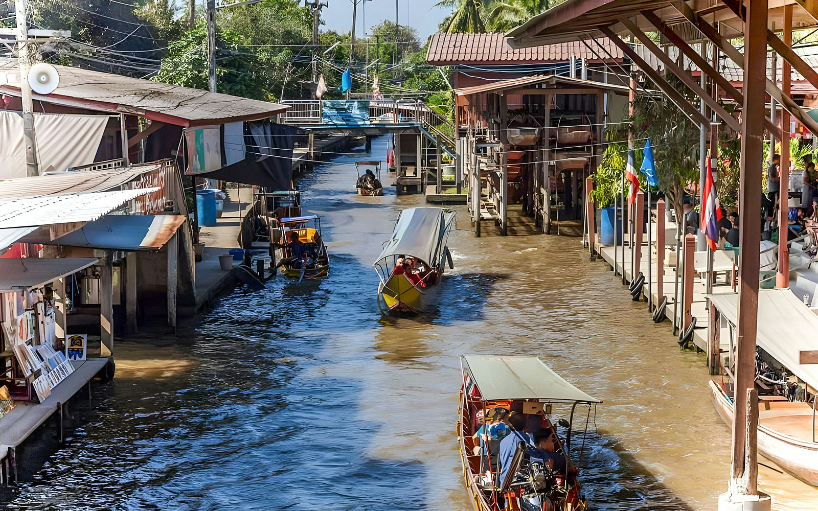 Boats at Damnoen Saduak Floating Market, Bangkok, with traditional Thai house in background.