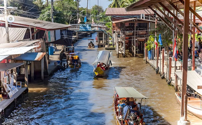 Boats navigating a bustling floating market canal with shops on both sides.