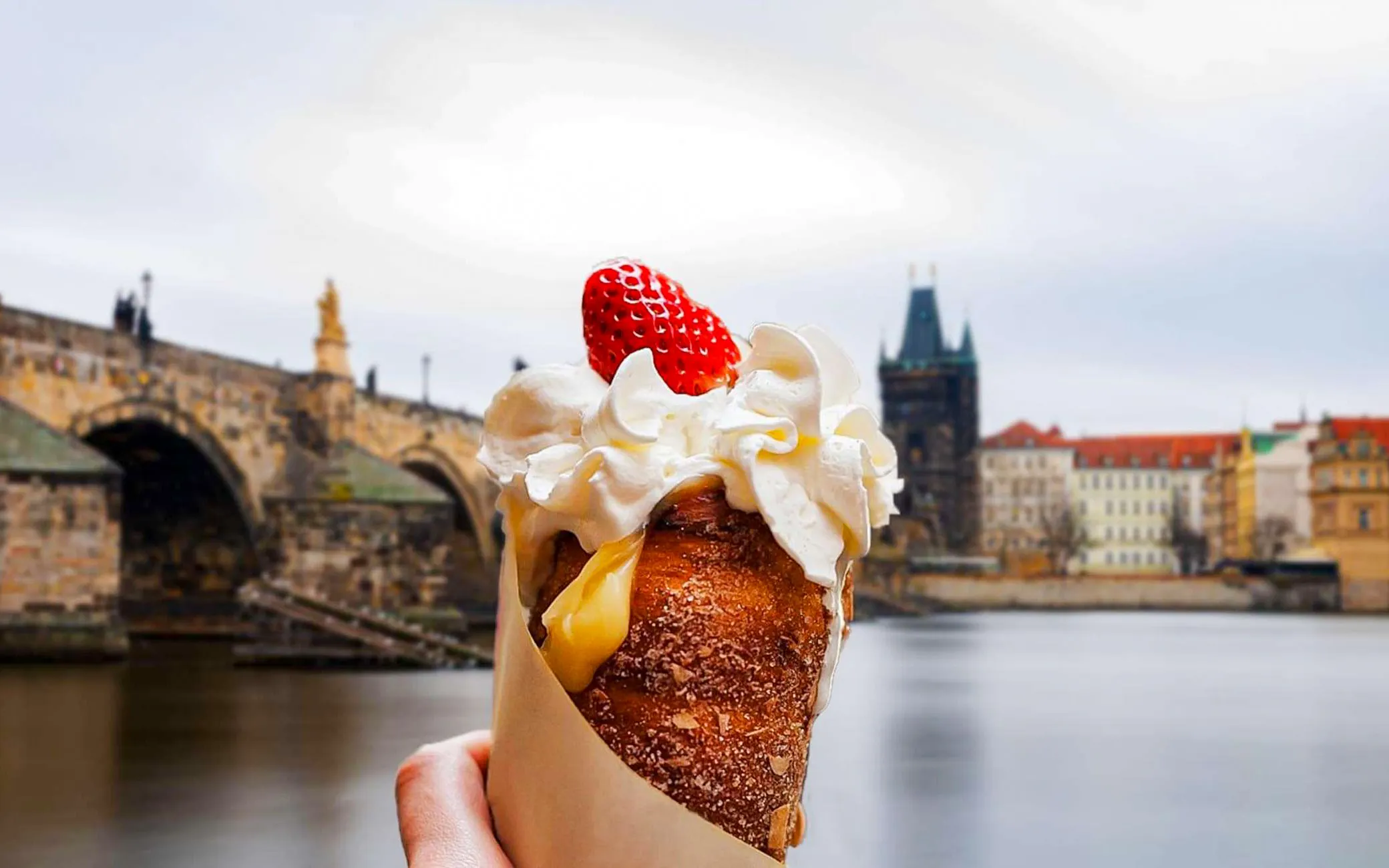 Trdelník with whipped cream and strawberry in front of Charles Bridge, Prague Old Town.