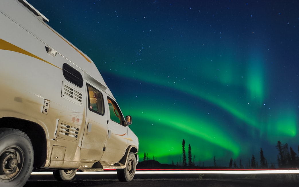 Van parked under Northern Lights in a starry night sky.