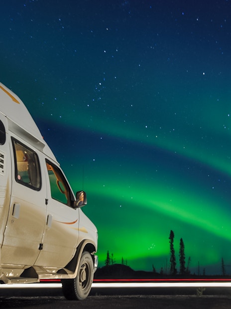 Van parked under Northern Lights in a starry night sky.