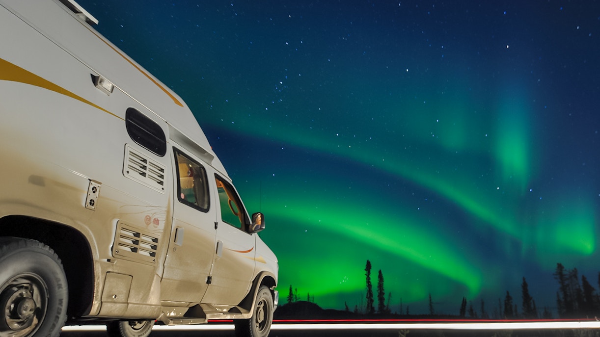 Van parked under Northern Lights in a starry night sky.
