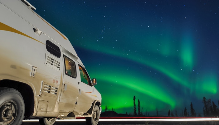 Van parked under Northern Lights in a starry night sky.
