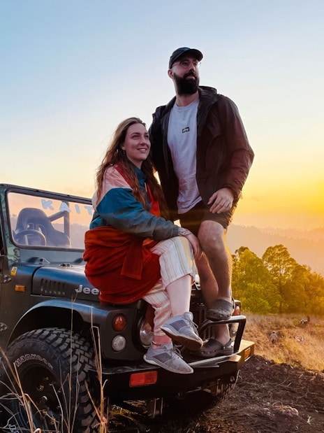 Couple on Jeep at sunrise, overlooking Bali landscape.
