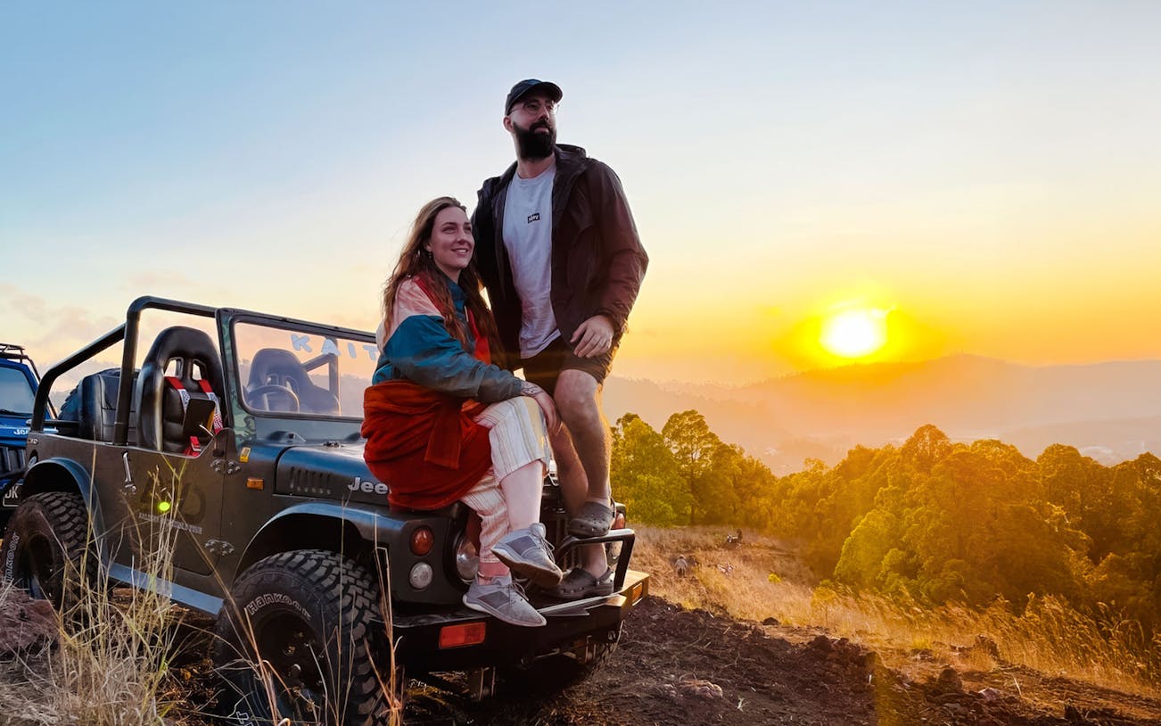 Couple on Jeep at sunrise, overlooking Bali landscape.