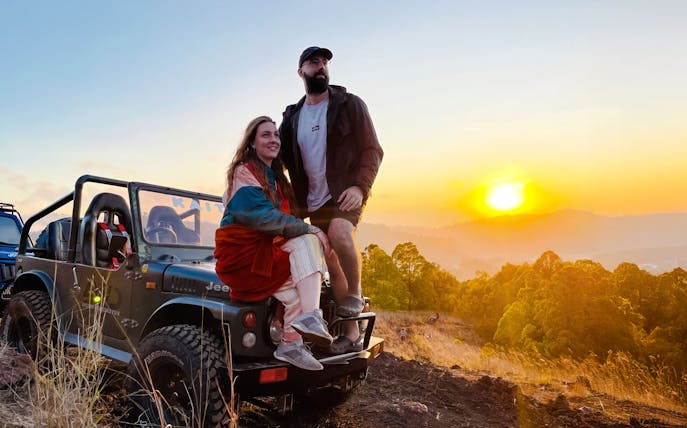 Couple on Jeep at sunrise, overlooking Bali landscape.