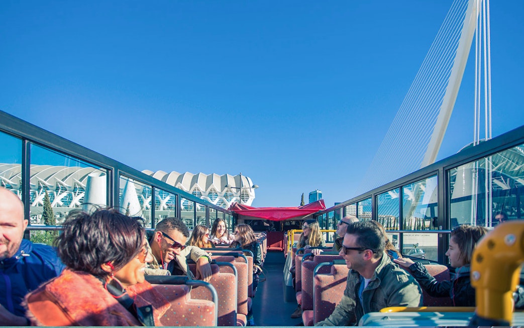 Open-top bus tour in Valencia with passengers enjoying views of modern architecture.