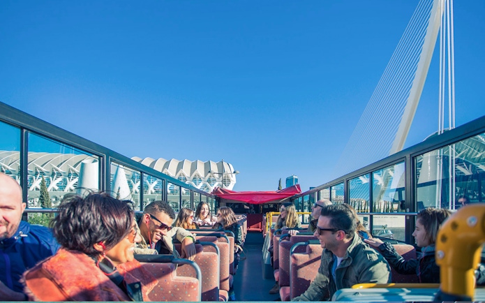 Open-top bus tour in Valencia with passengers enjoying views of modern architecture.