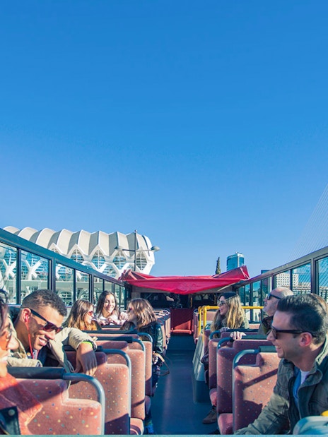 Open-top bus tour in Valencia with passengers enjoying views of modern architecture.