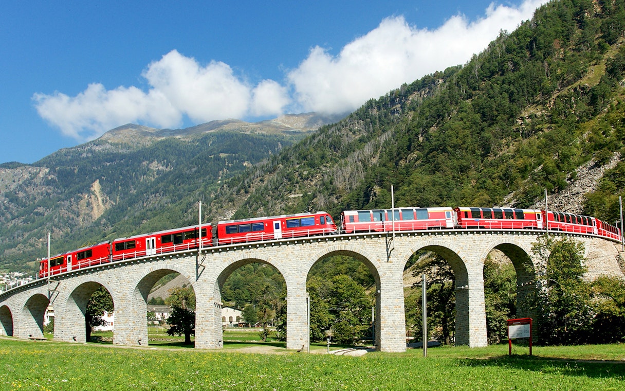 Bernina Express on Brusio Circular Viaduct with mountain backdrop.