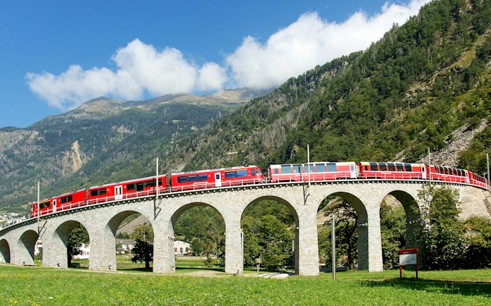 Bernina Express on Brusio Circular Viaduct with mountain backdrop.