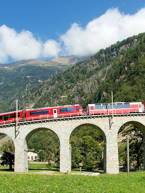 Bernina Express on Brusio Circular Viaduct with mountain backdrop.