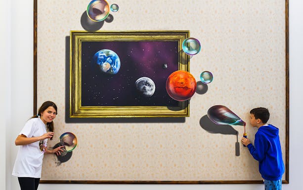 Visitors interacting with 3D space-themed art at Illusion Art Museum, Prague.