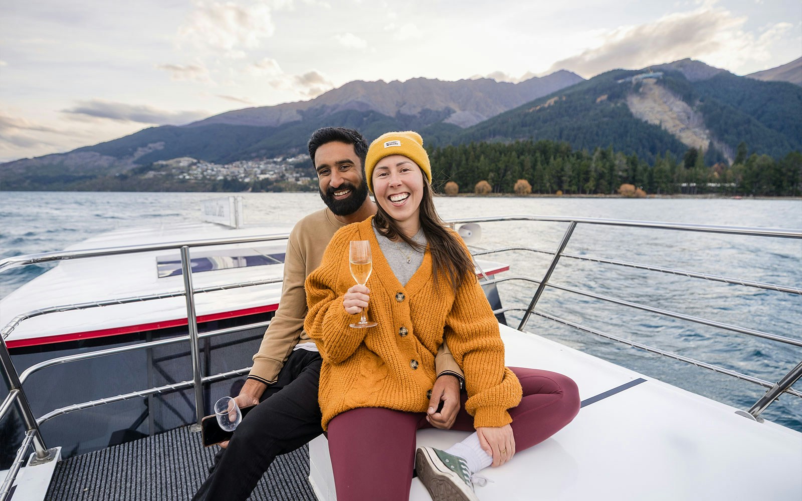 Couple enjoying wine on a boat with Queenstown mountains in the background on Lake Wakatipu.